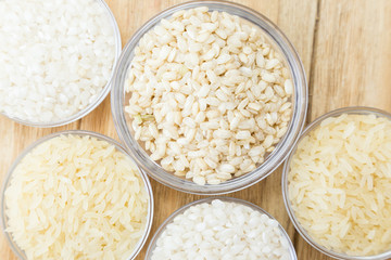 three kinds of uncooked rice in glass bowls on a wooden table
