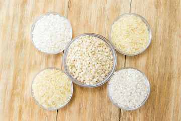 three kinds of uncooked rice in glass bowls on a wooden table
