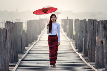 Burmese woman holding traditional red umbrella and walking on U Bein Bridge