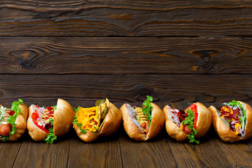 lot of big delicious hot dogs with sauce and vegetables on wooden background.