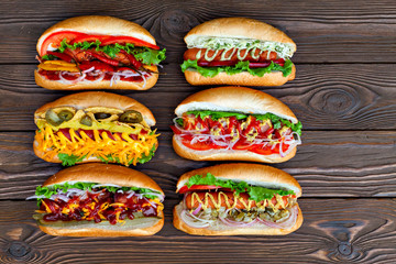 lot of big delicious hot dogs with sauce and vegetables on wooden background.