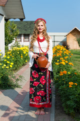 Obraz premium woman in national ukrainian traditional costume holding a clay jug and welcoming guests