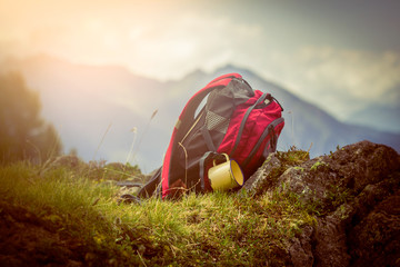Outing trip in the mountains Austria Alps with closeup backpack mug cup what lying on the green grass and rocks and sunshine