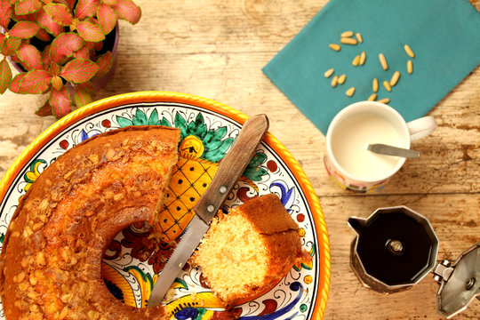 Breakfast with homemade ciambellone, milk, coffee. A plant, a blue napkin and some pine nuts.
