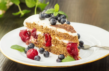 Piece of sweet cake with cherry, blueberry and mint