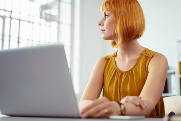 frau arbeitet am notebook und schaut in gedanken zum fenster