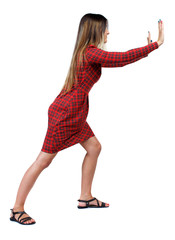 back view of woman pushes wall.  Isolated over white background. Rear view people collection. backside view of person. The girl in red plaid dress stands sideways and pushing his hands something to
