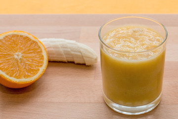 Orange and banana smoothie in glass on orange background
