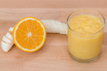 Orange and banana smoothie in glass on orange background