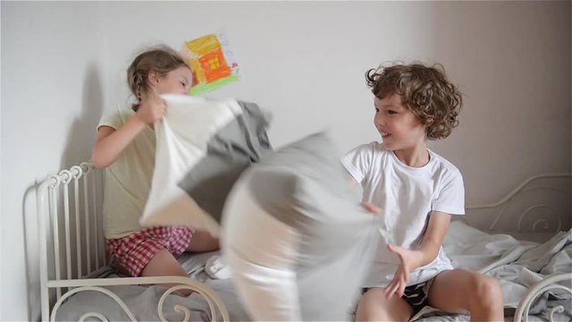 The brother and the sister have arranged fight by pillows on a bed in a bedroom.