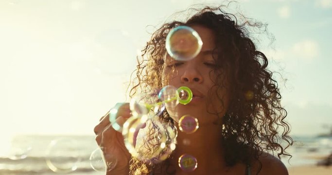Happy young woman blowing bubbles on the beach at sunset