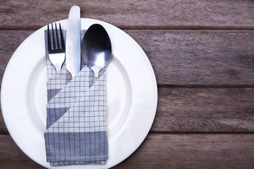 Top view of a white plate with cutlery in a grey with white check on a wooden table.