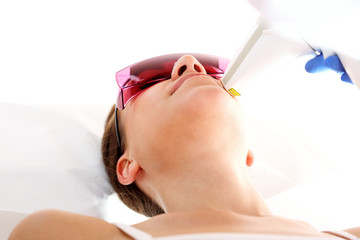 Klinika kosmetyczna, kobieta podczas zabiegu depilacji laserowej twarzy - obrazy, fototapety, plakaty