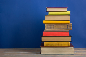 Old hardback Books on grunge wooden table desk shelf in library. Back to school background with copy space for your ad text. No labels, blank spine