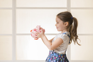 Portrait of happy young little girl looking at her pink piggy bank. Education, school and money...