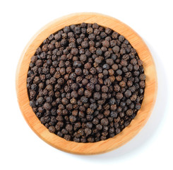 dried black peppers in the wooden plate, top view