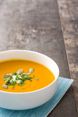 Pumpkin soup and pumpkin seeds on rustic wooden background

