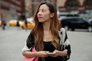 Young Asian woman in city texting cell phone

