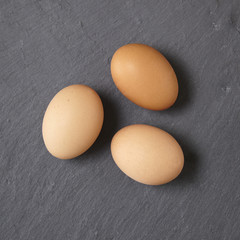 Three brown chicken eggs on a rustic slate background