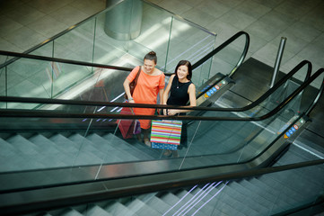 Two darkhaired young girlfriend on the escalator in shopping center.