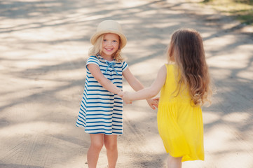 two little girls are spinning holding hands,dancing and laughing in the summer on the street