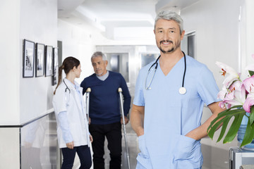 Confident Doctor Standing With Colleague And Patient In Backgrou
