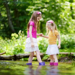 Two cute little sisters playing in a river wearing raining boots