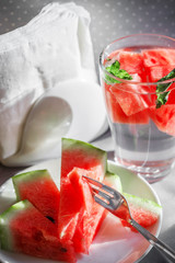 Slices of watermelon on white plate and in glass with water. Napkins at background. Healthy food concept.