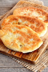 Delicious cakes cooked of unleavened dough and fried in vegetable oil in a frying pan. Pies on a cutting board. Old wooden background. Closeup