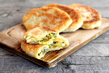 Fried cakes stuffed with mushrooms, hard-boiled eggs, green onions and dill on a wooden board. Delicious breakfast, picnic, snack idea. Unleavened dough recipe