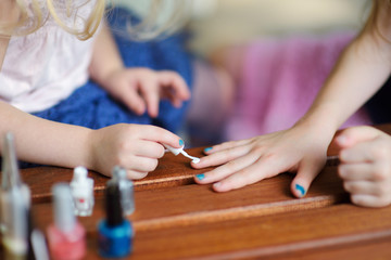 Adorable little girls having fun playing at home with colorful nail polish doing manicure and painting nails © MNStudio