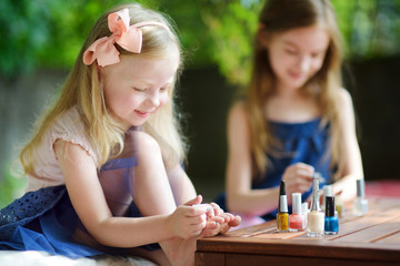 Obraz na płótnie Canvas Adorable little girls having fun playing at home with colorful nail polish doing manicure and painting nails