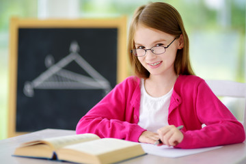 Smart little schoolgirl with pen and books writing a test in a classroom