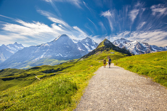 Fototapeta Young couple hiking in panorama trail leading to Kleine Scheidegg from Mannlichen with Eiger, Monch and Jungfrau mountain (Swiss Alps) in the background, Berner Oberland, Grindelwald, Switzerland. 