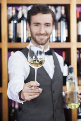 Bartender Offering White Wine Glass Against Shelves
