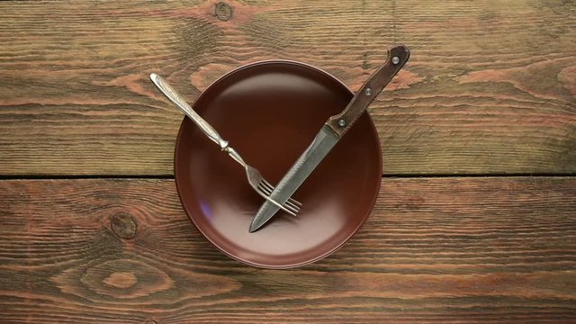 Brown empty dinner plate with fork and knife on wooden table 
