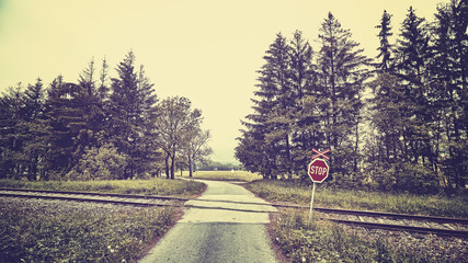 Vintage toned stop sign at railway crossing in a rural landscape.