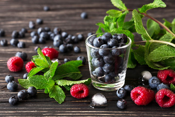 Blueberries, raspberries and mint at black wooden table.