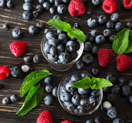 Blueberries, raspberries and mint at black wooden table.