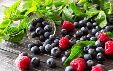 Blueberries, raspberries and mint at black wooden table.