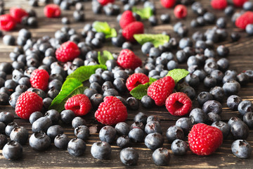 Blueberries, raspberries and mint at black wooden table.