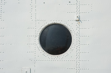 photographed close-up of metal siding and porthole in military plane in gray
