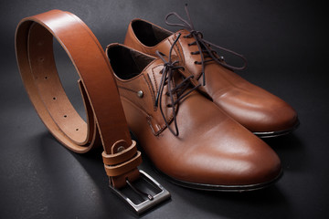 Selective focus of men's leather belt and shoe on wooden table