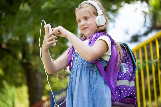 cute little school-girl listening to music outside with white he