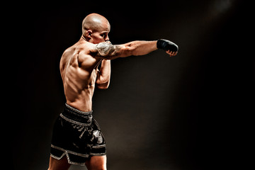 Muscular kickbox or muay thai fighter punching in darkness