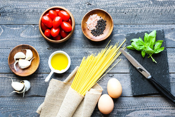 Top view of italian ingredients for tomato and basilic spaghetti with olive oil and garlic over a wood background.