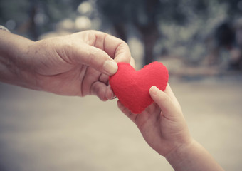 old hands holding young hand of a baby with red heart