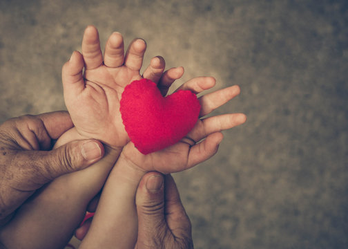 old hands holding young hand of a baby with red heart