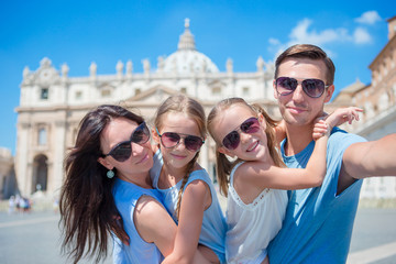 Happy young family taking selfie at St. Peter's Basilica church in Vatican city, Rome. Happy travel parents and kids making selfie photo picture on european vacation in Italy.