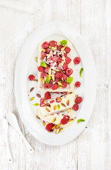 Homemade semifreddo with pistachio and raspberry in oval dish over white painted wooden background, top view, vertical composition